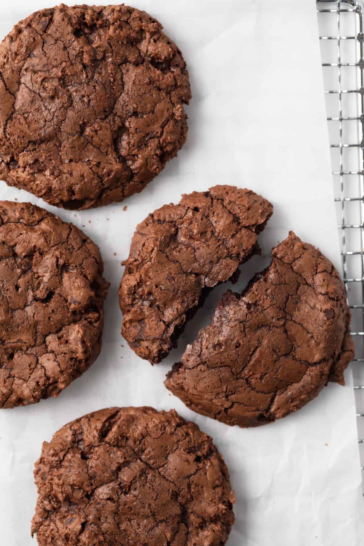 overhead of four brownie cookies with one split in half on white parchment paper