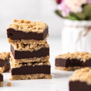 three chocolate oatmeal bars stacked next to flowers in vase and more oat bars