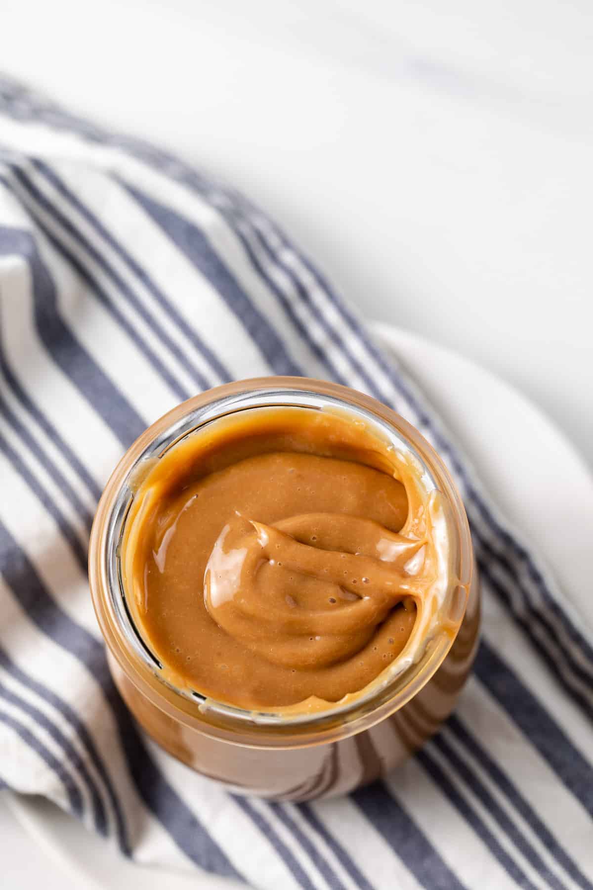 overhead of dulce de leche in glass jar with blue and white napkin