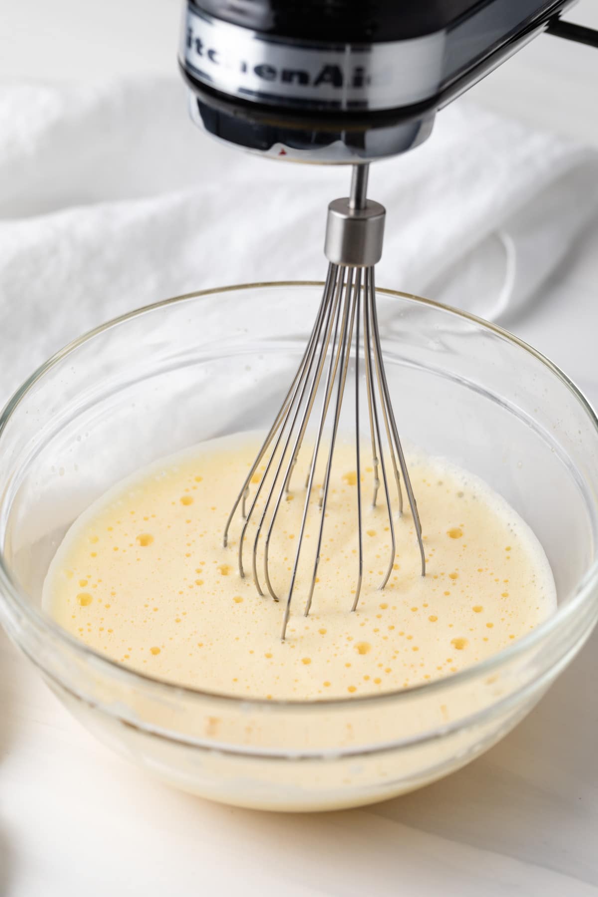 hand mixer with whisk attachment whipping eggs in glass bowl