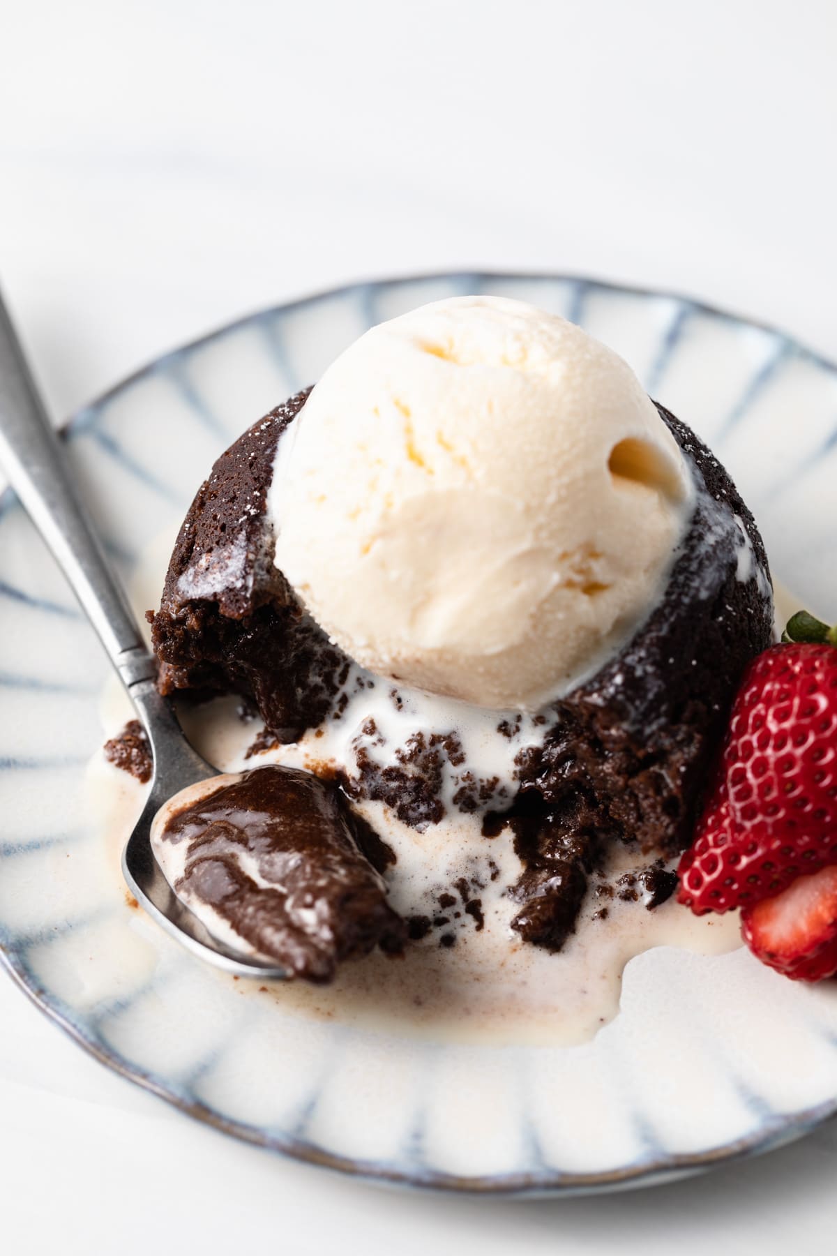 angled view of lava cake topped with ice cream and a spoon taking a bite out