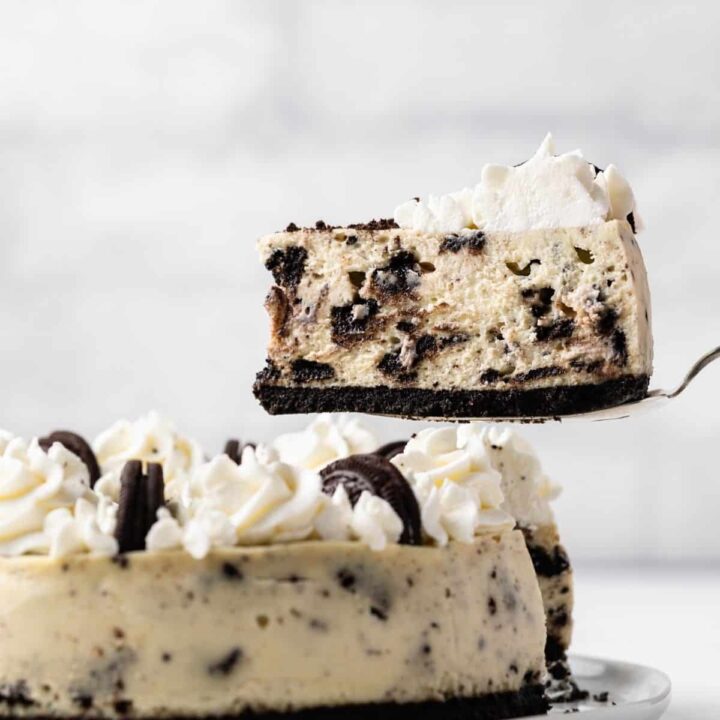 side view of slice of oreo cheesecake being taken out and held above whole cheesecake