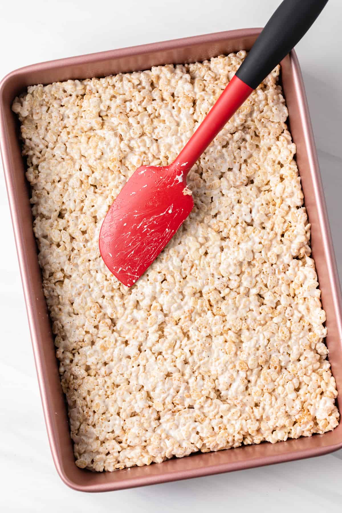 rice krispie treat mixture pressed into pink pan with red spatula