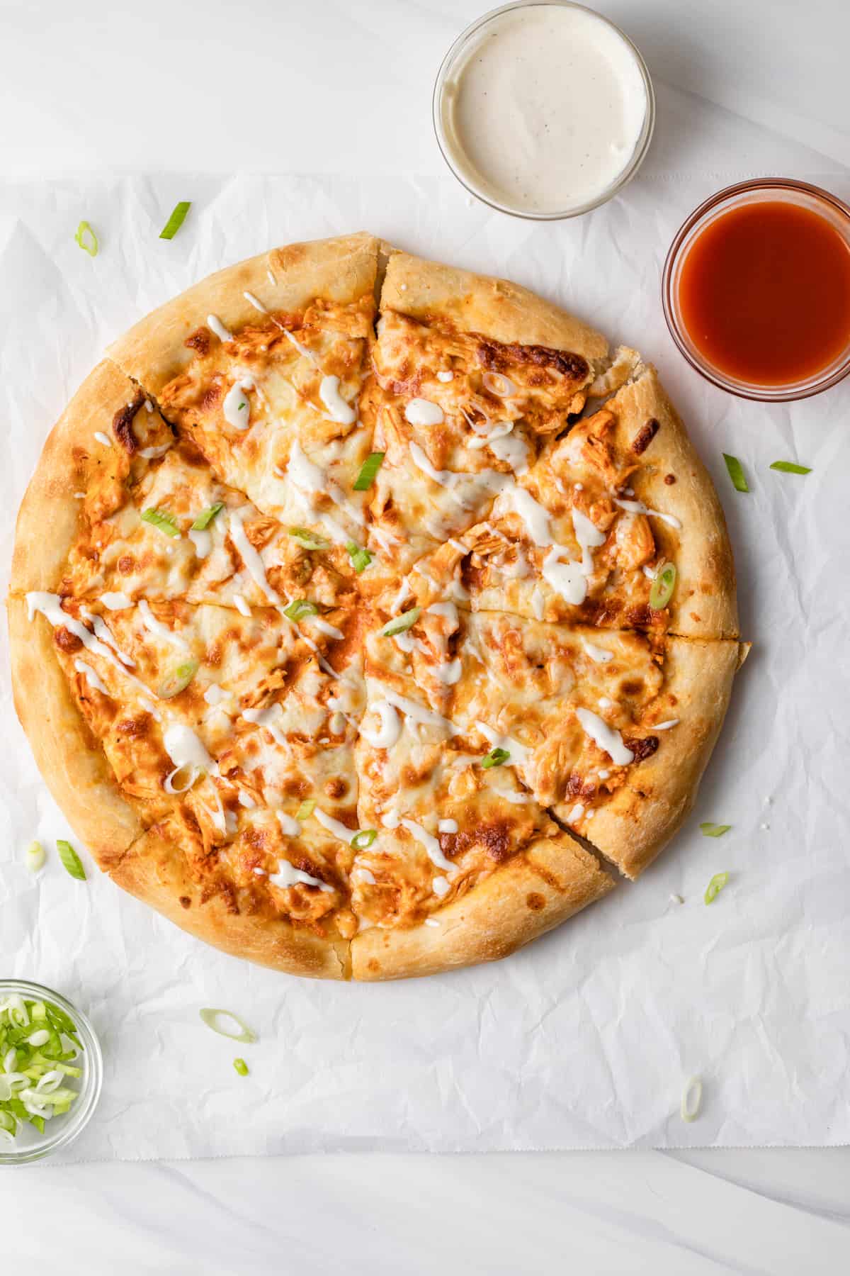 overhead view of buffalo chicken pizza cut into slices on white parchment paper