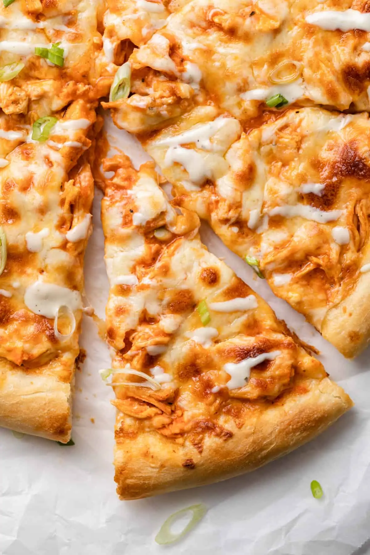 slice of buffalo chicken pizza slightly pulled away from whole pizza on white parchment paper