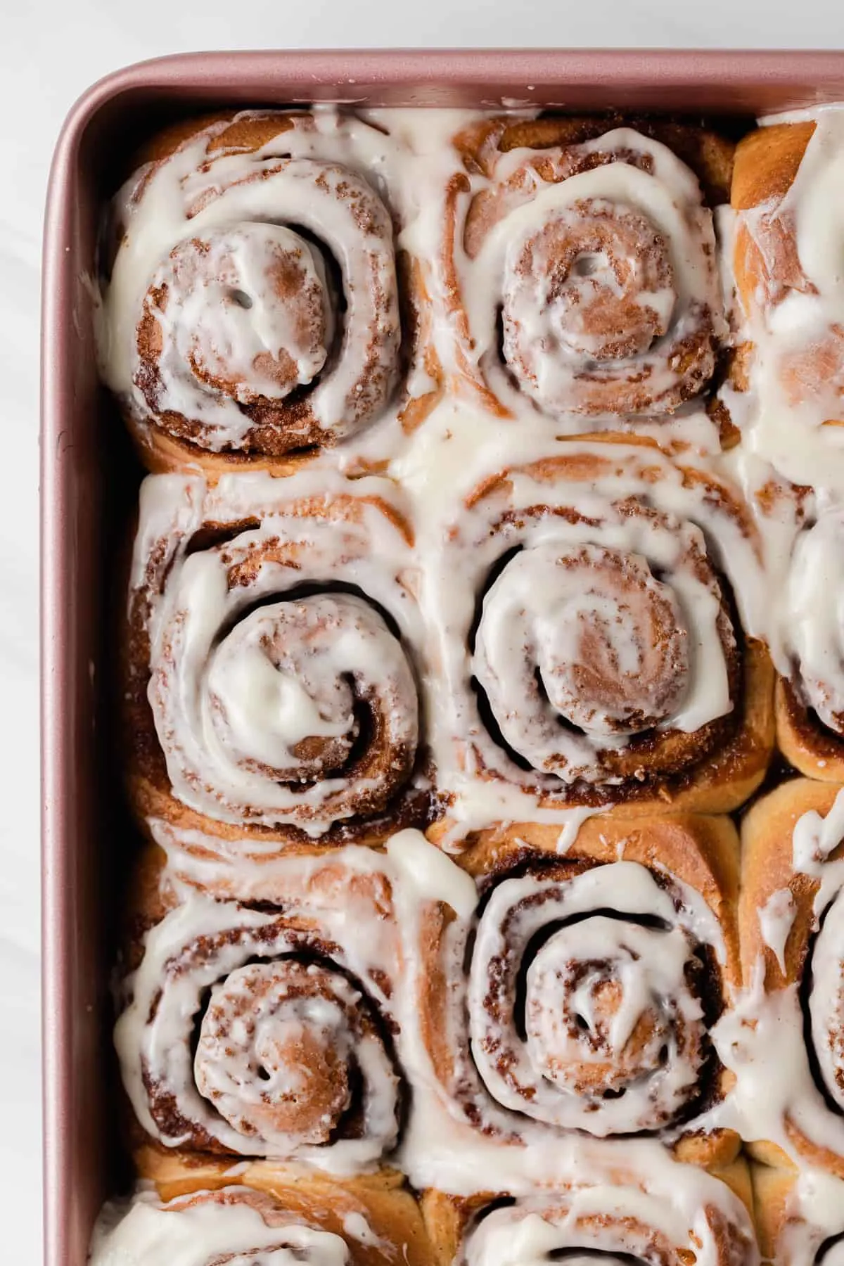 overhead of iced cinnamon rolls in a pink baking pan