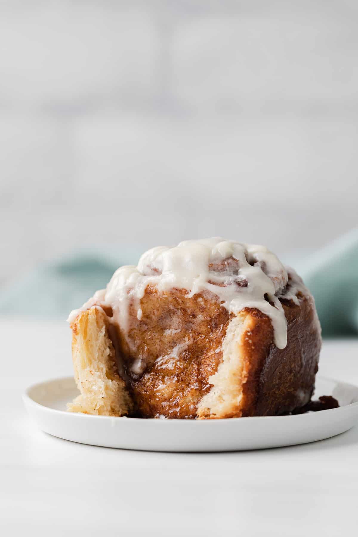 side view of a single cinnamon roll on a white plate with teal napkin behind