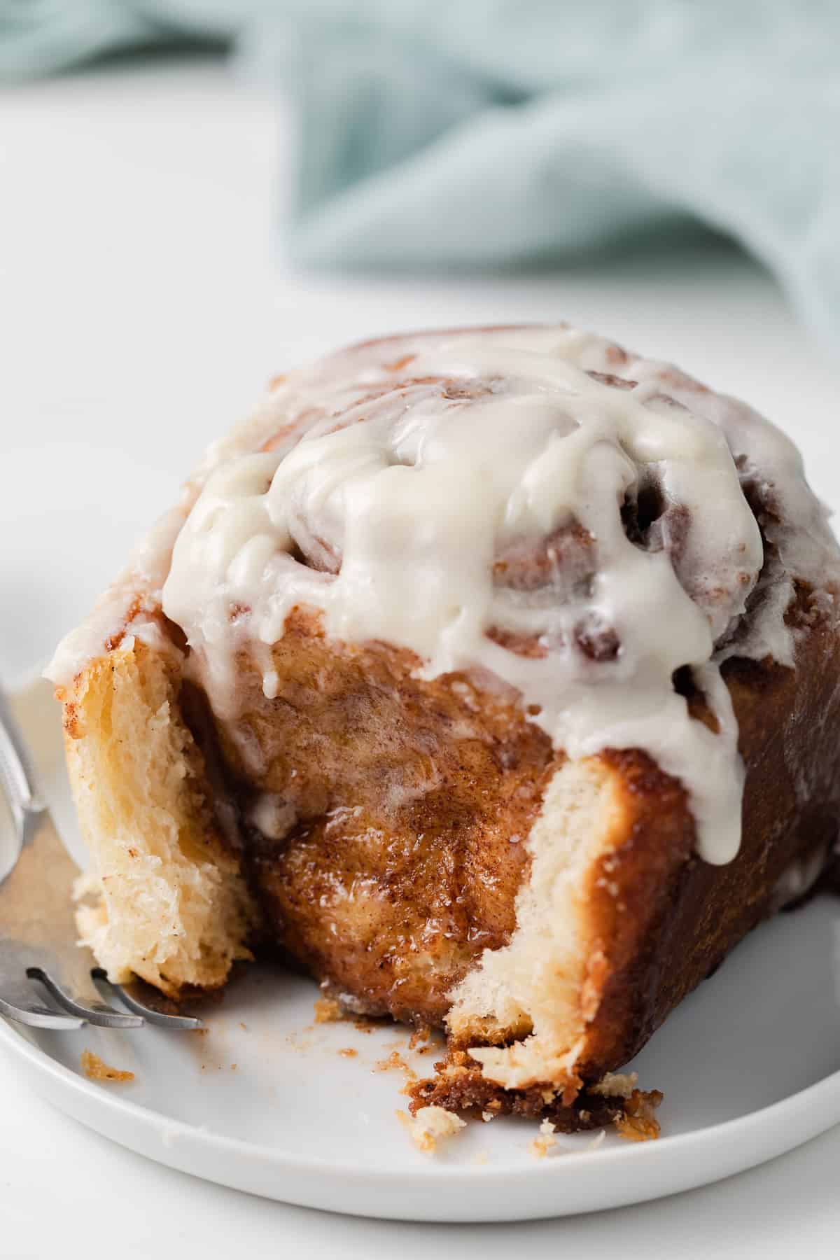 close up of an iced cinnamon roll with a bite taken out on a white plate