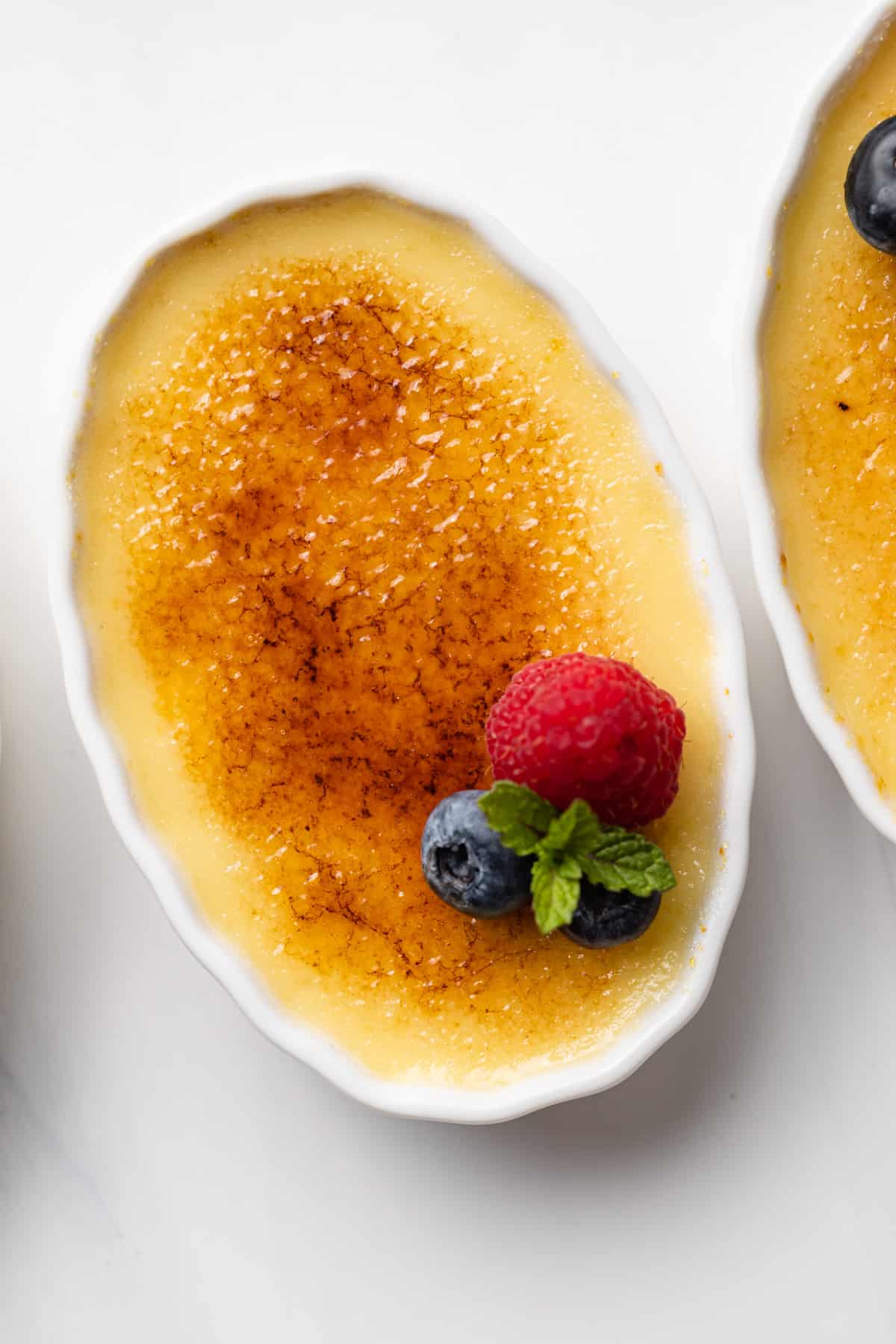 close up of creme brulee in an oval ramekin with fresh berries and mint