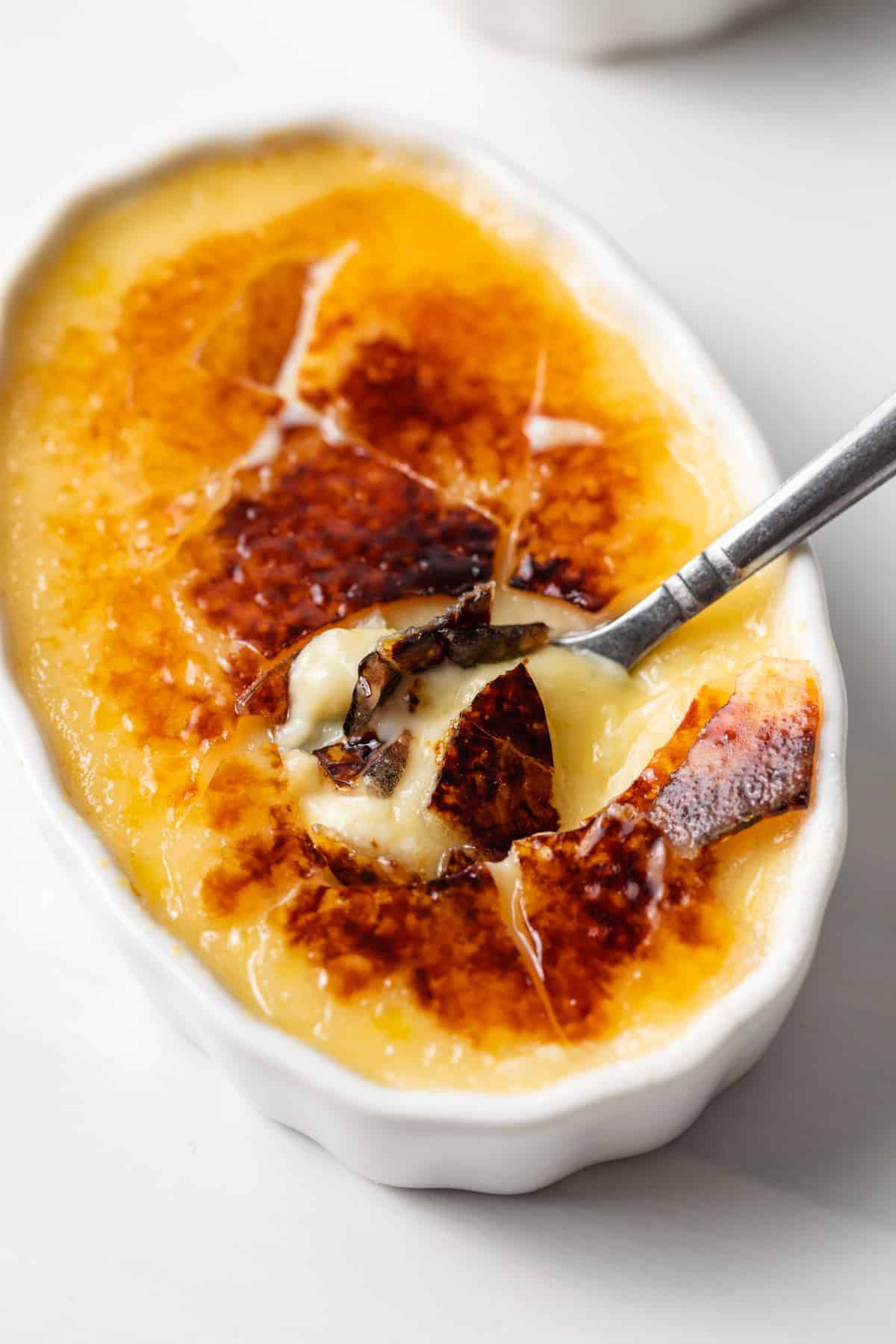 angled view of a spoon cracked through the sugar layer on top of a ramekin of creme brulee