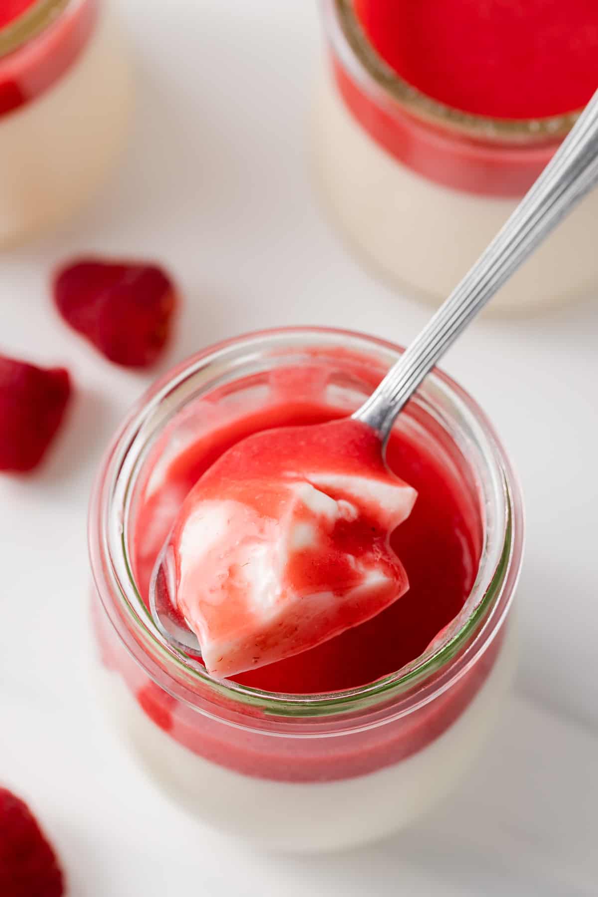 overhead view of a spoon taking out a bite of panna cotta with fresh raspberry sauce