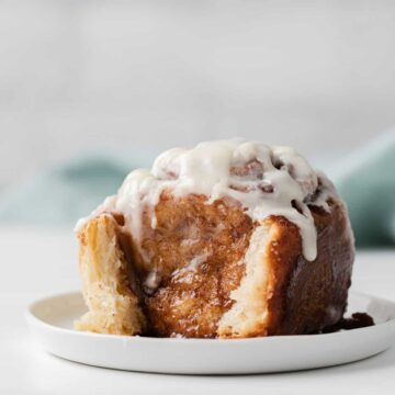 side view of a single cinnamon roll on a white plate with teal napkin behind