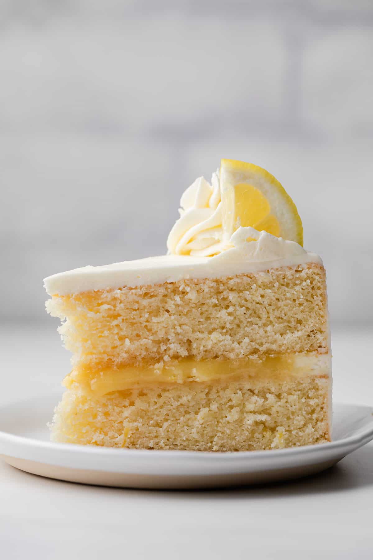 slice of lemon cake filled with lemon curd and topped with lemon buttercream on a white plate