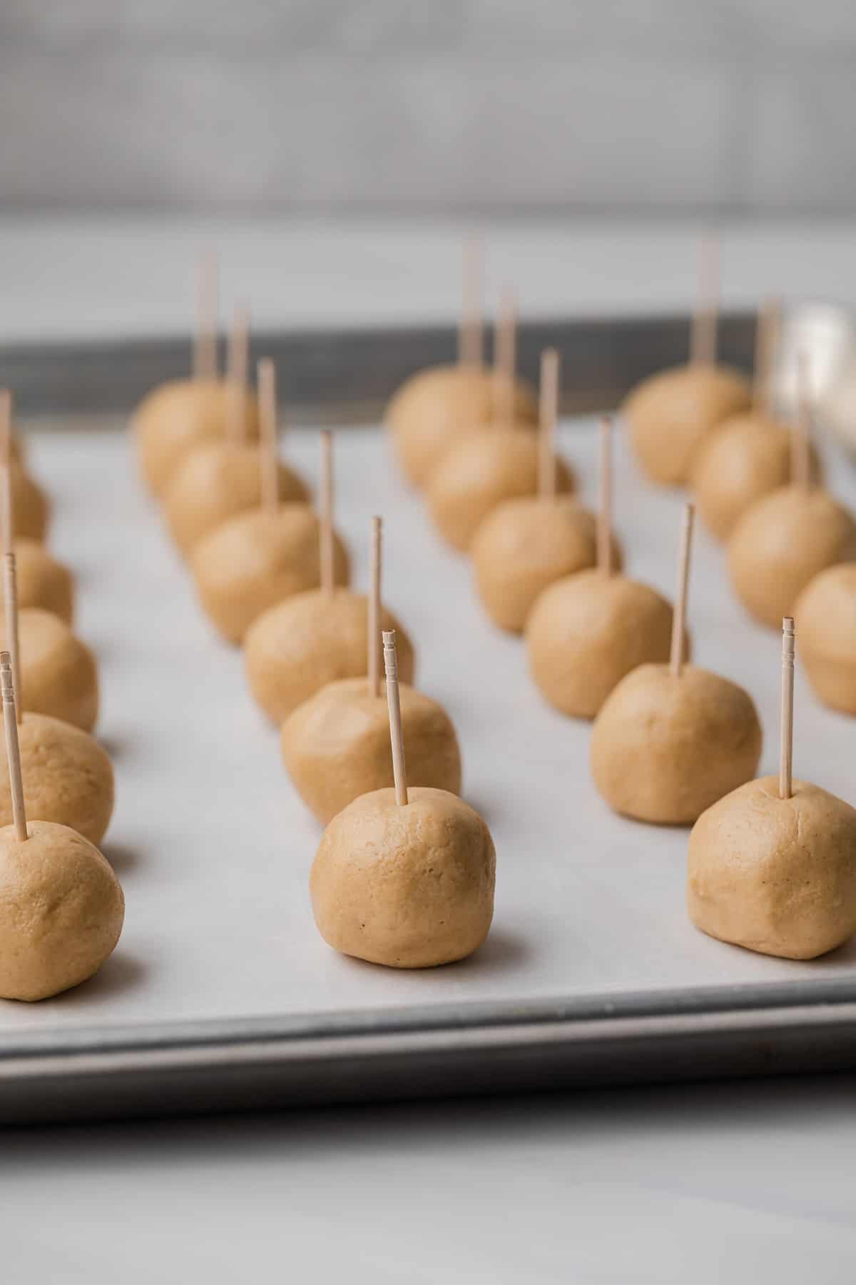 peanut butter balls with toothpicks sticking out of the top lined neatly on a baking sheet