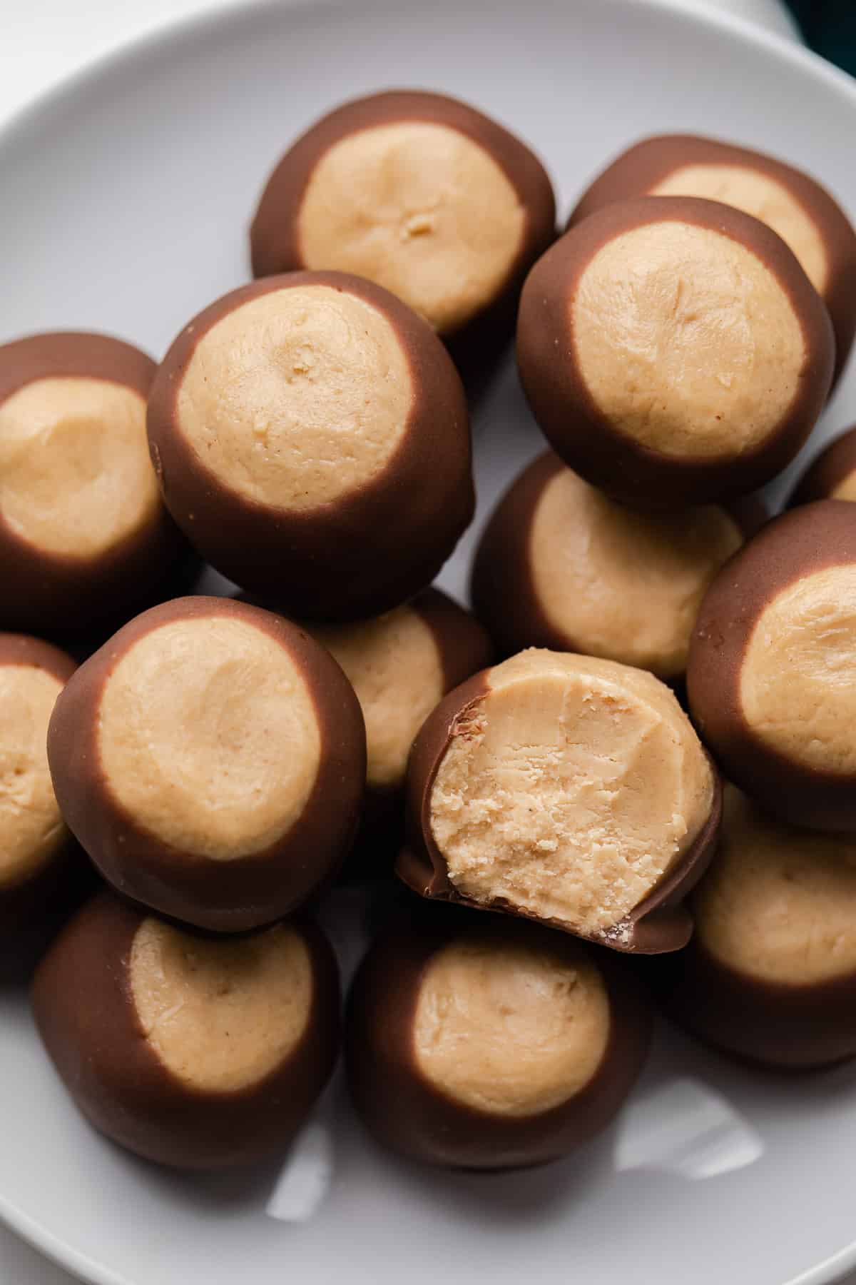 Close up of buckeye candy on a white plate with a bite taken out so the inside is visible