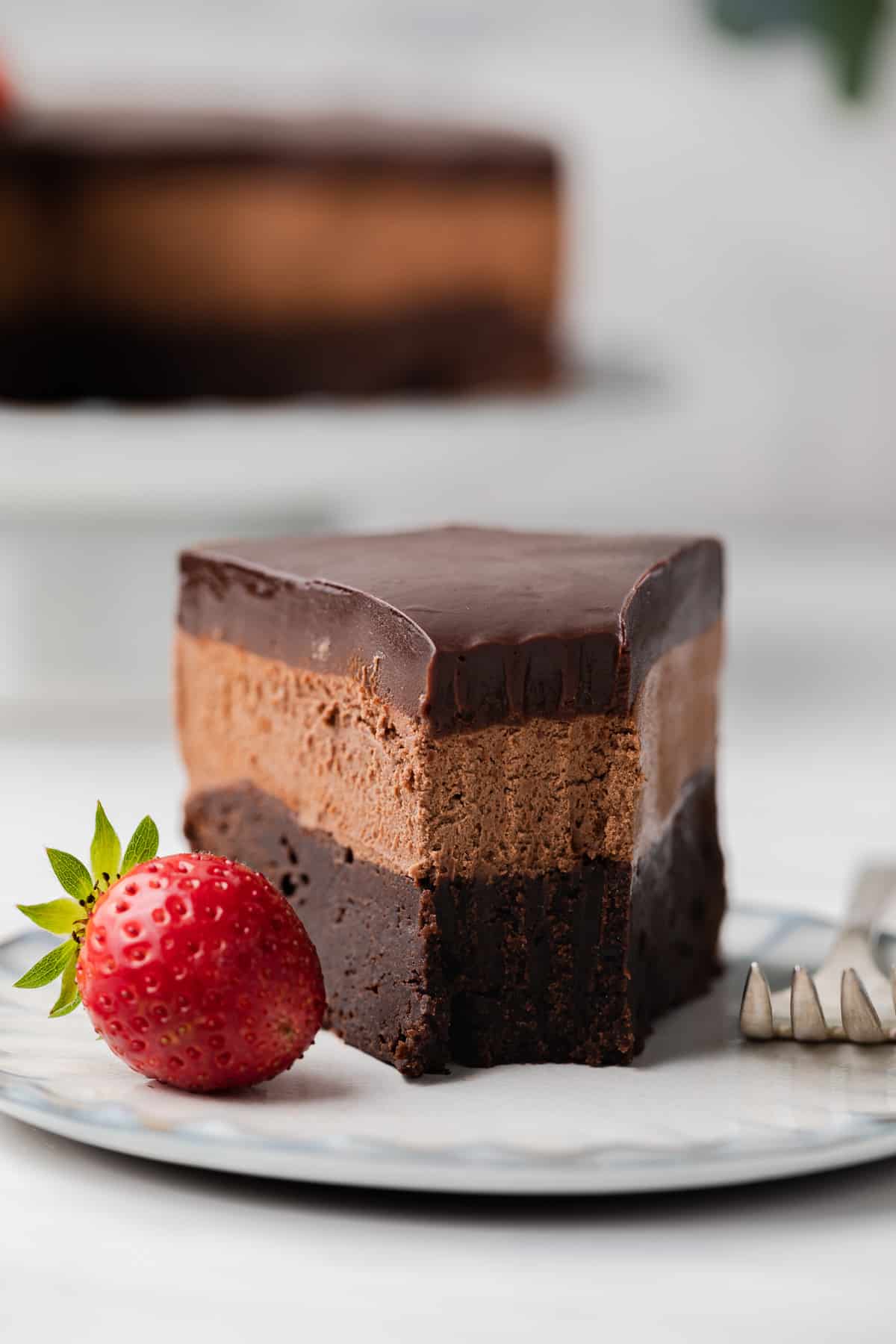 Slice of three layer mousse cake on white plate with a bite taken out.