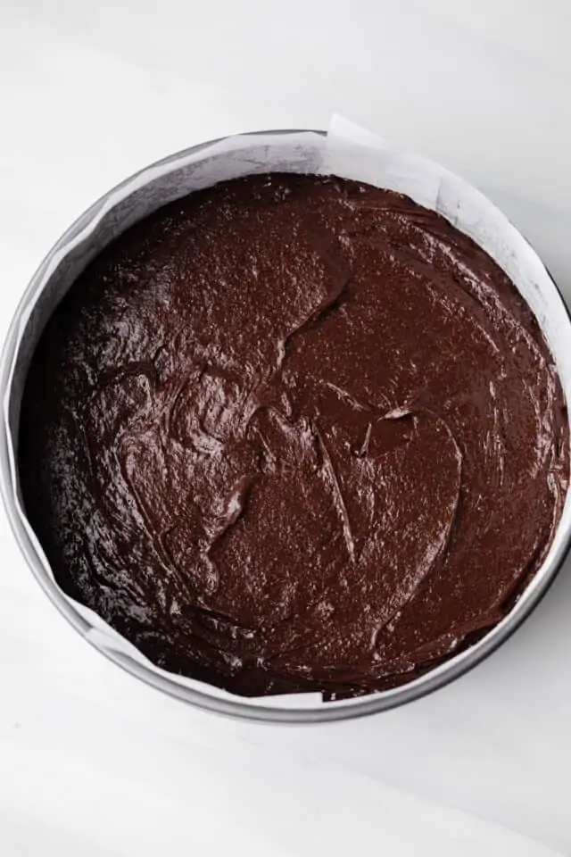 Brownie batter in a round pan lined with parchment paper.