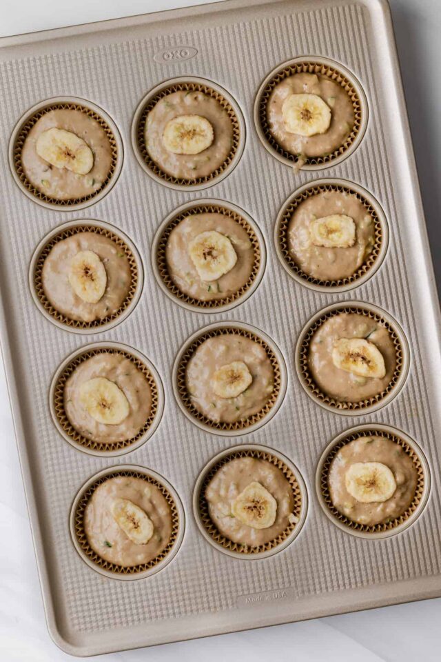 Muffin batter in muffin pan topped with banana chips.