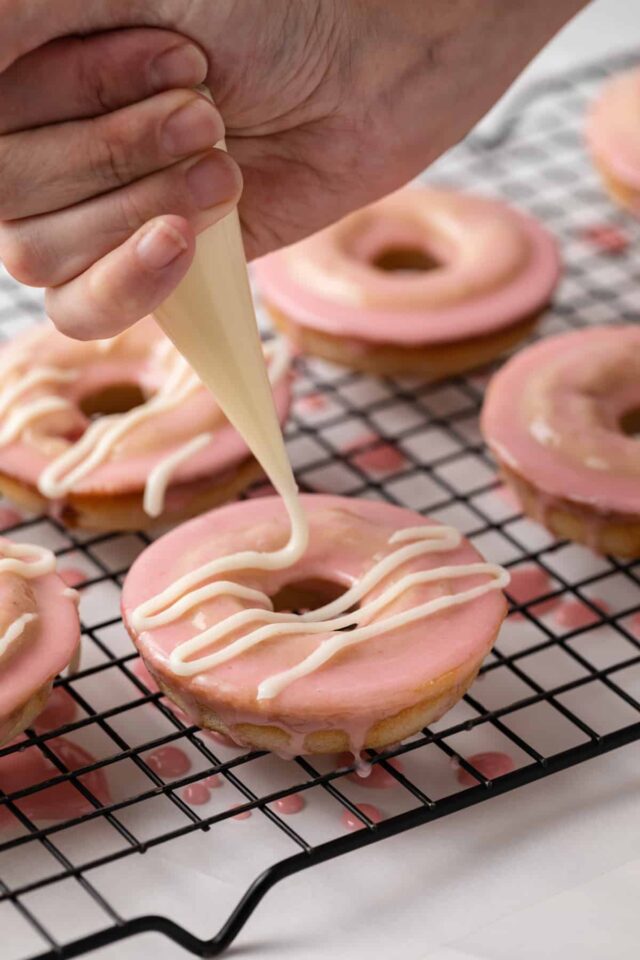 Cream cheese glaze drizzled over glazed strawberry donuts