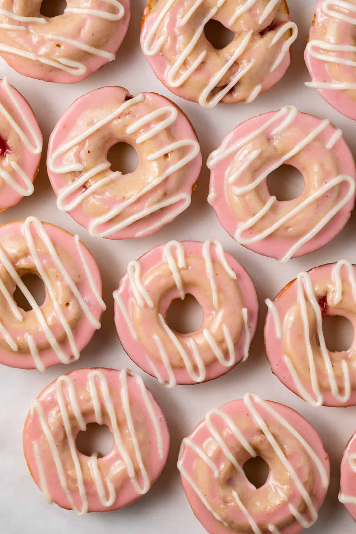 Baked strawberry donuts with frosting on white parchment paper