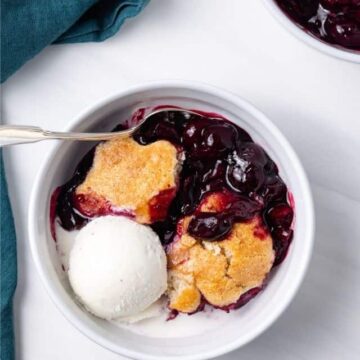 A white bowl of cherry cobbler with a scoop of ice cream