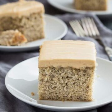 A slice of Easy Banana Cake recipe topped with luscious brown sugar frosting on a white plate.