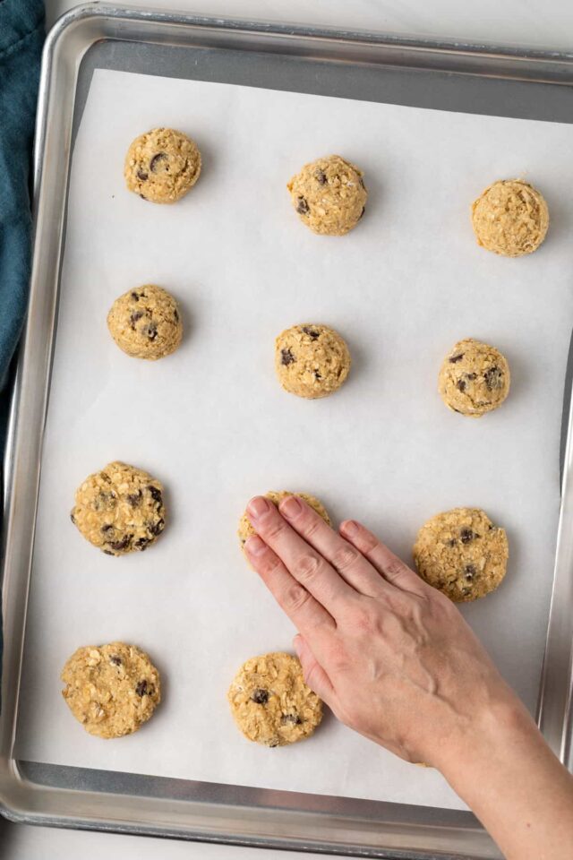 A hand pressing down on balls of chocolate chip cookie dough