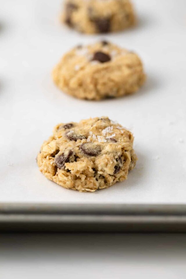 Flattened oatmeal chocolate chip cookie dough on a baking sheet with sea salt