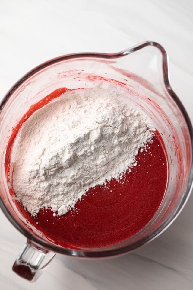 Flour added to wet ingredients in a glass bowl.