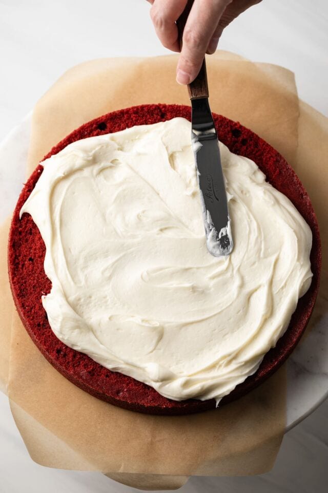 Cream cheese frosting being spread over single cake layer
