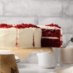 Slice being taken out of red velvet cake with cream cheese frosting.