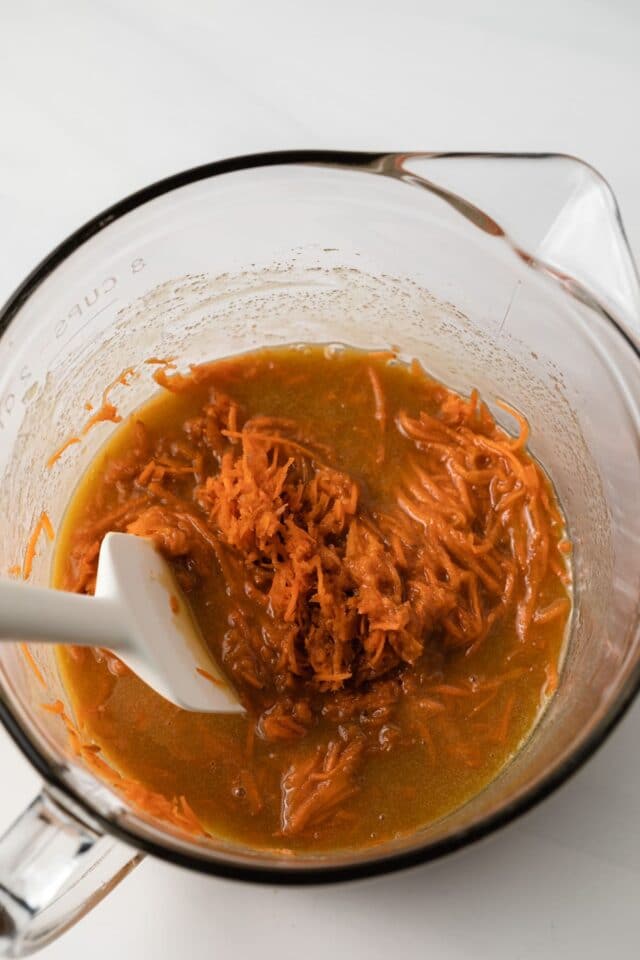 Carrot added to wet ingredients in a glass bowl.