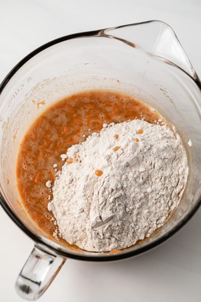 Flour added to wet ingredients in glass bowl.