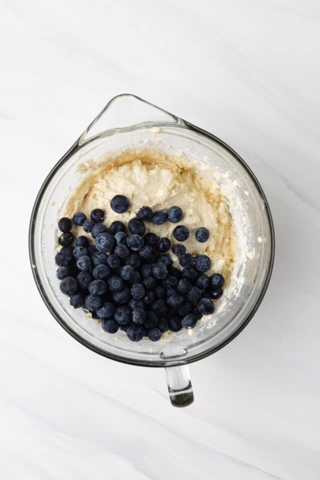 Muffin batter with blueberries in glass bowl.