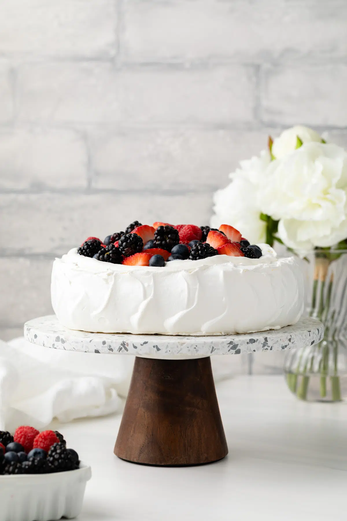 Pavlova on cake stand topped with whipped cream and berries.