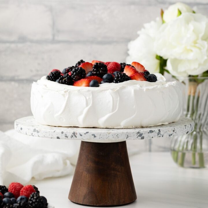 Pavlova on cake stand topped with whipped cream and berries.