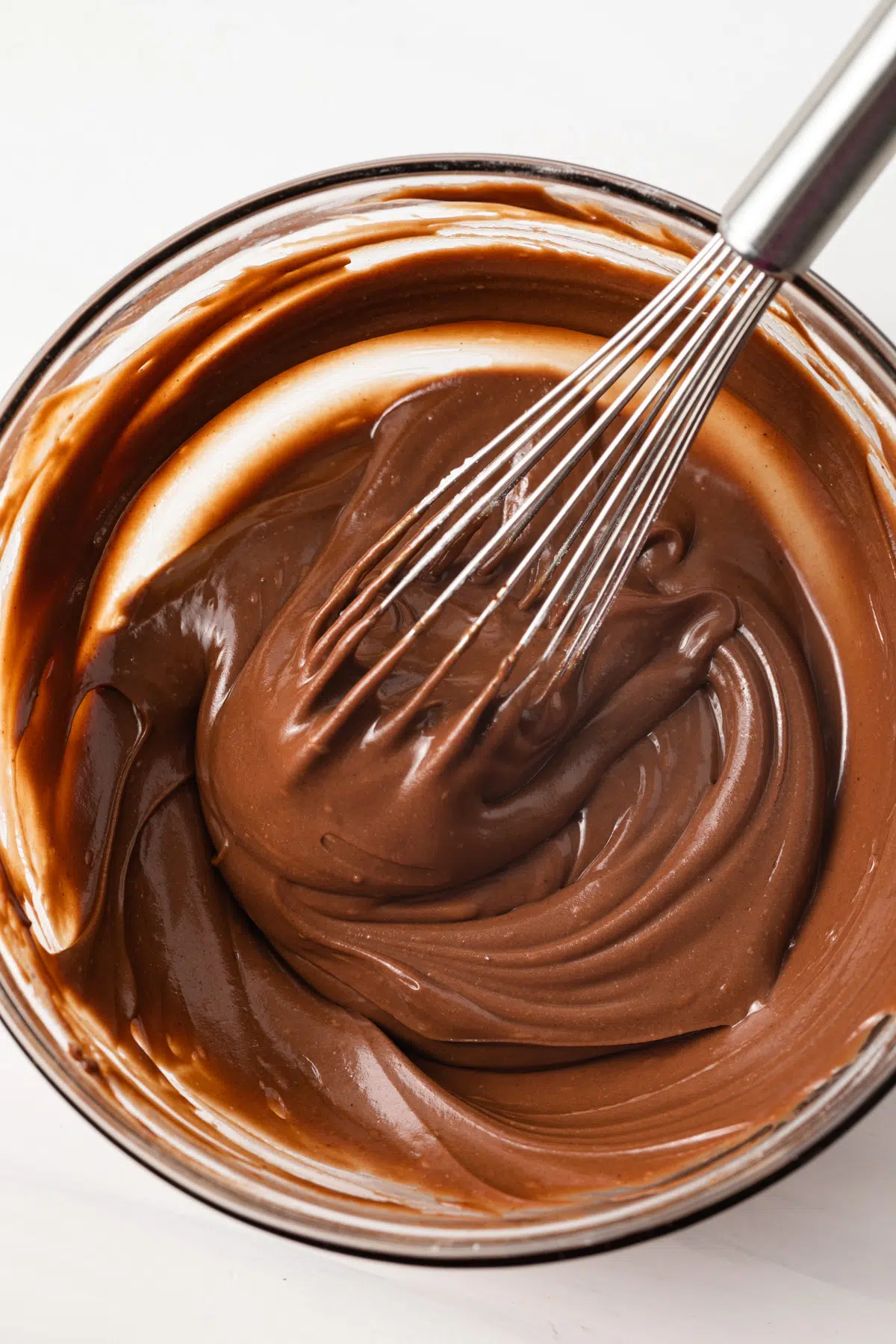 Chocolate glaze in bowl with whisk.