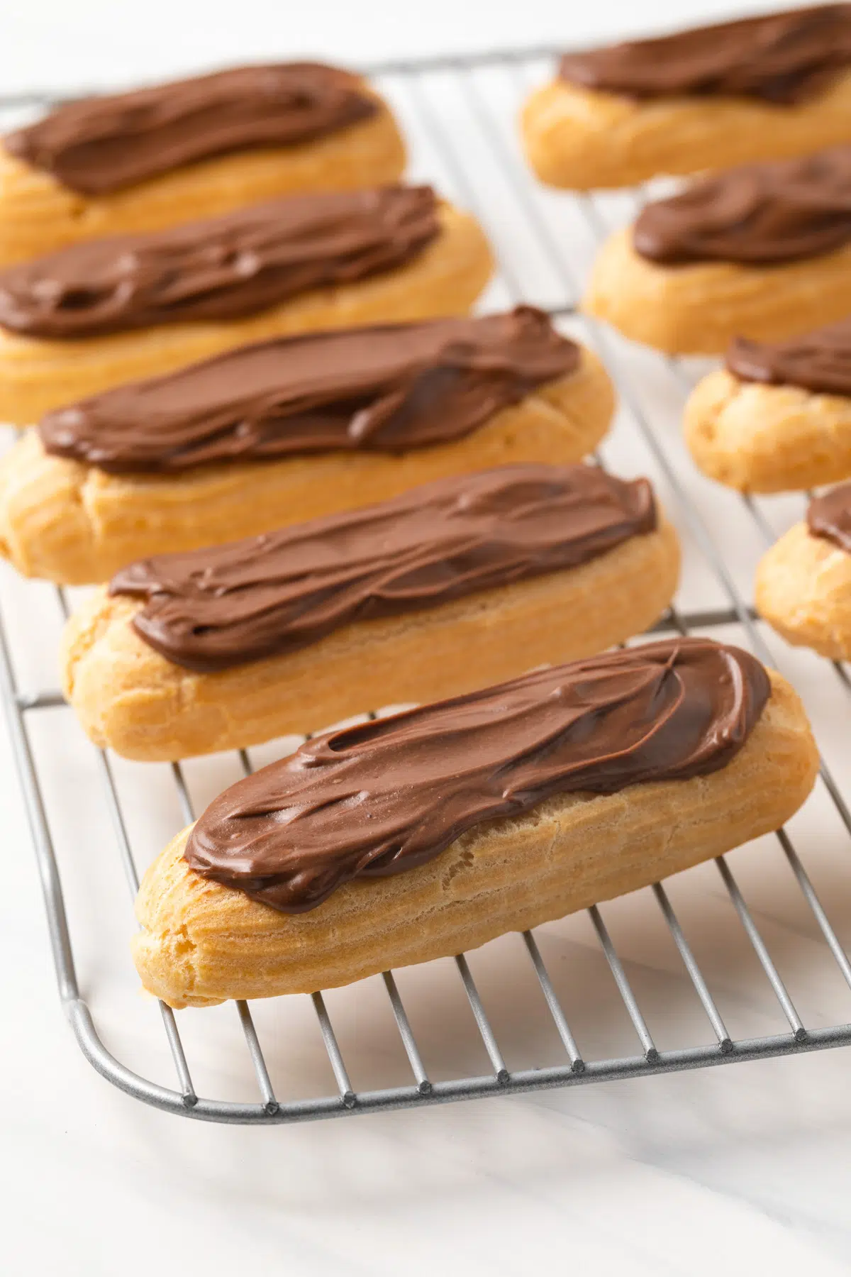 Homemade chocolate eclairs on wire rack.