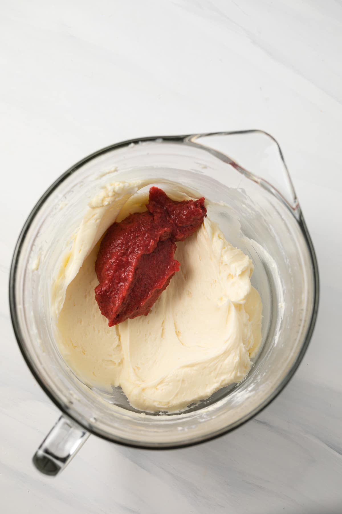 Buttercream frosting with strawberry puree in glass bowl.