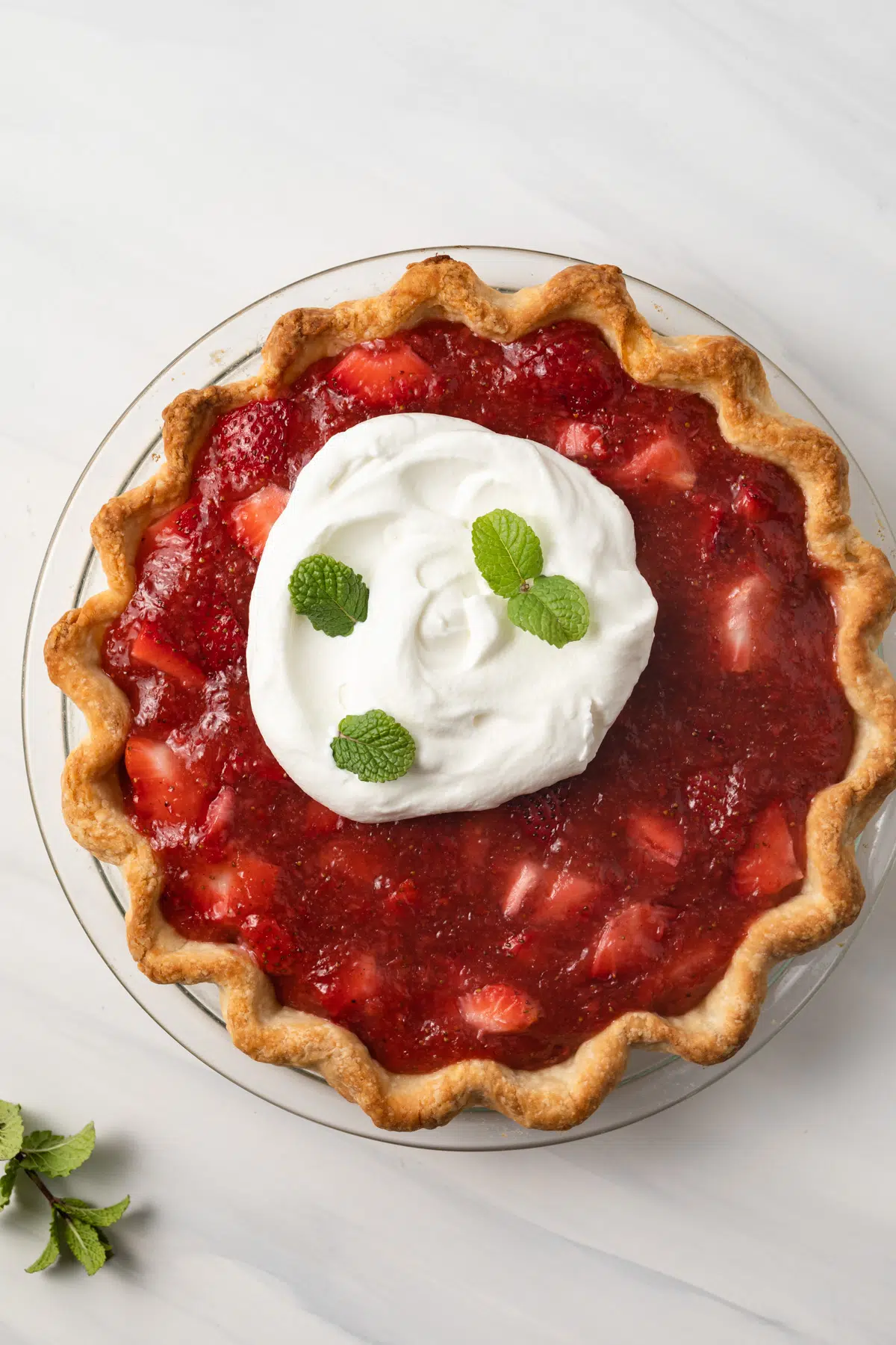 Strawberry pie topped with whipped cream and mint leaves.