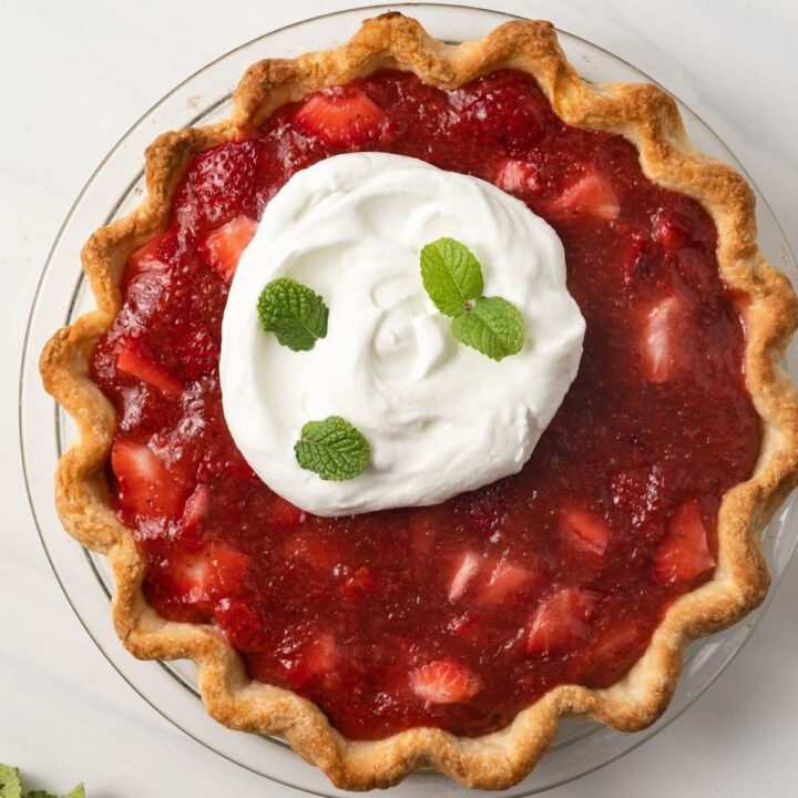 Strawberry pie topped with whipped cream and mint leaves.