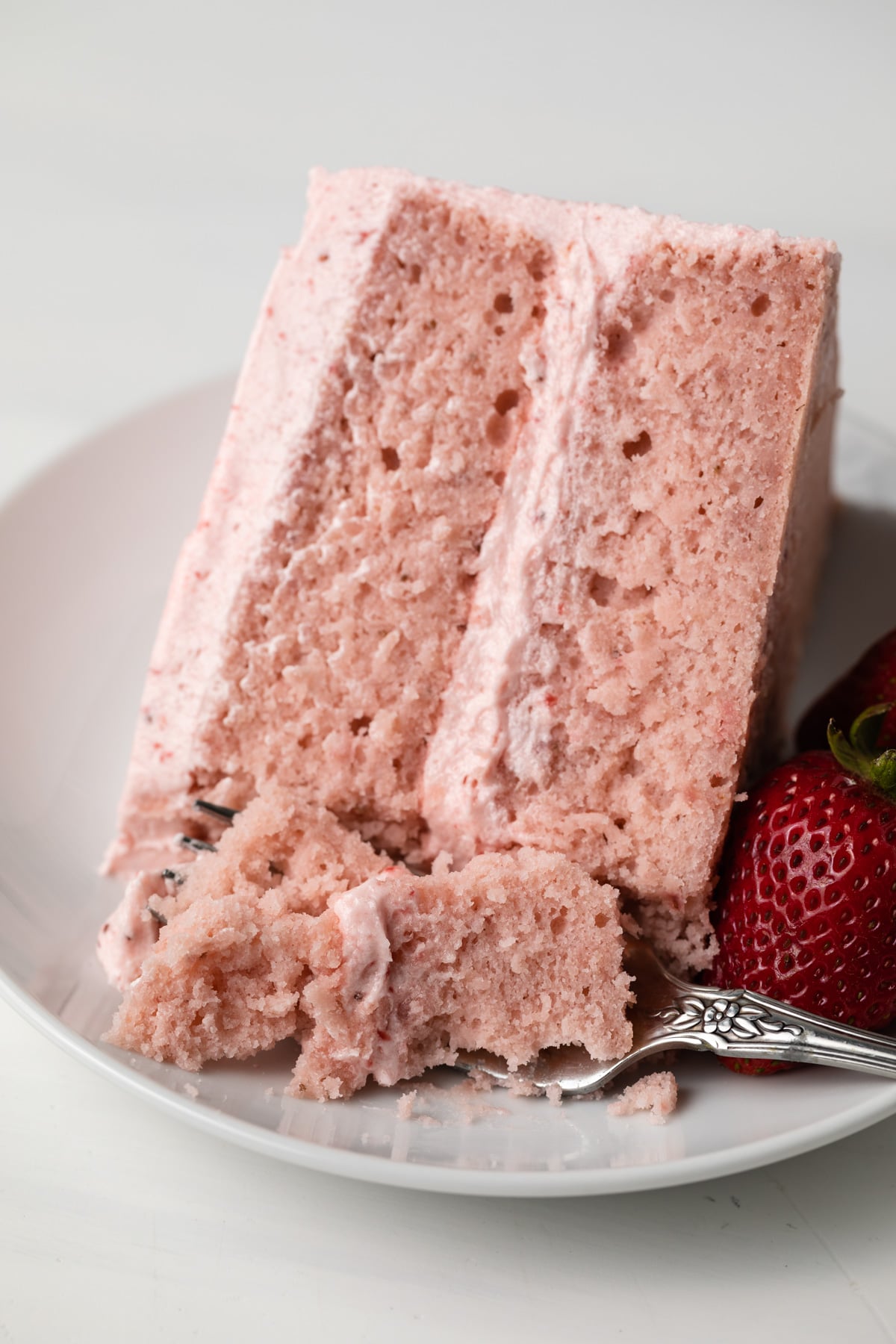 Slice of strawberry cake with fork taking a bite out.