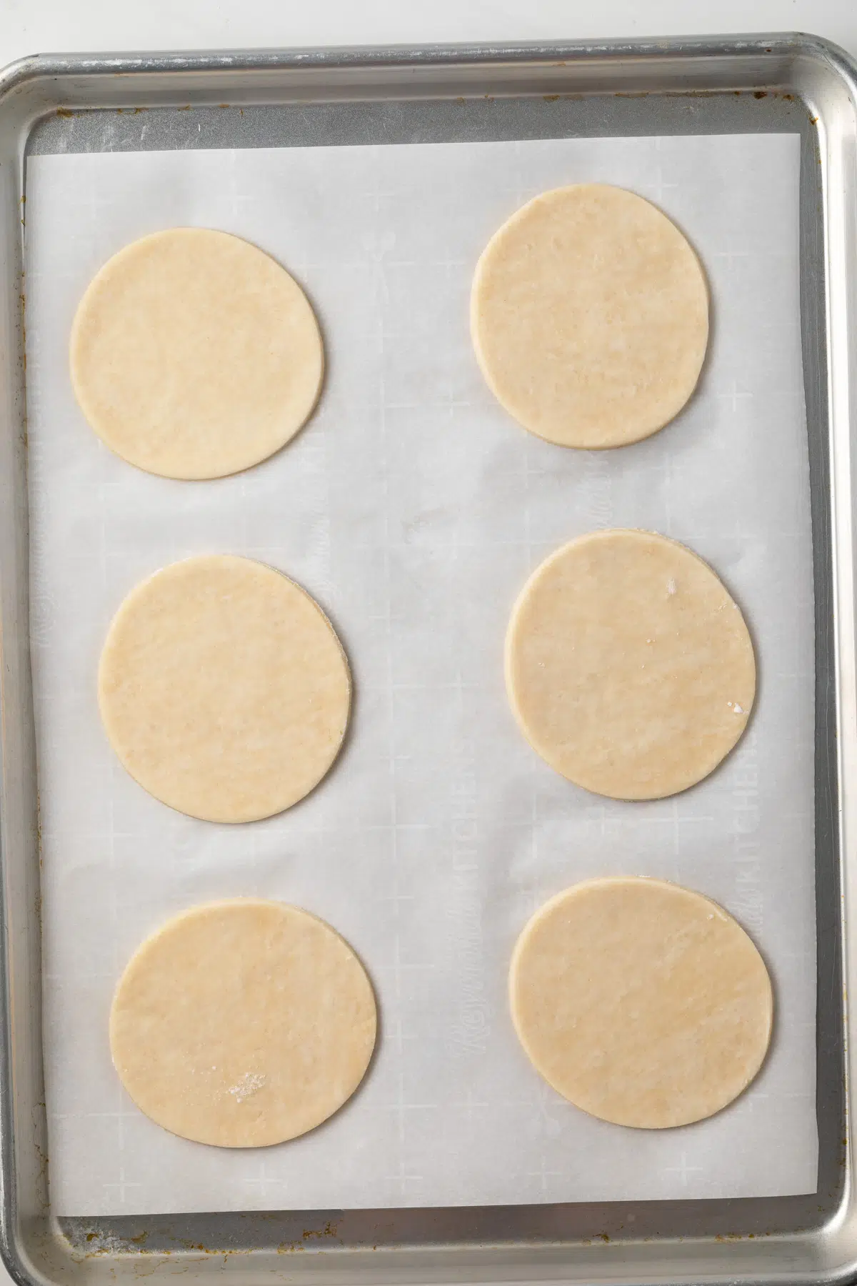 Six mini pie dough circles on a baking sheet.