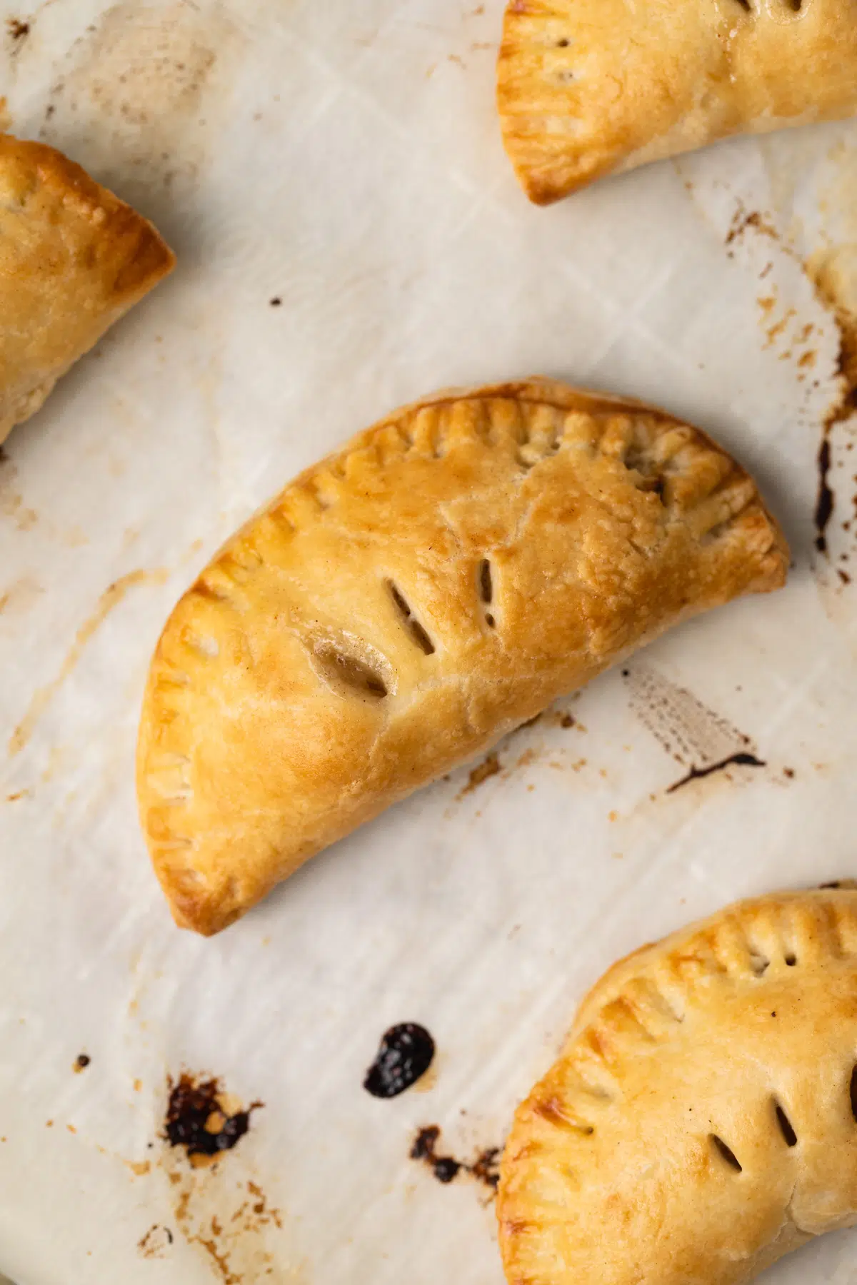 Baked mini apple pies on baking sheet with parchment paper.