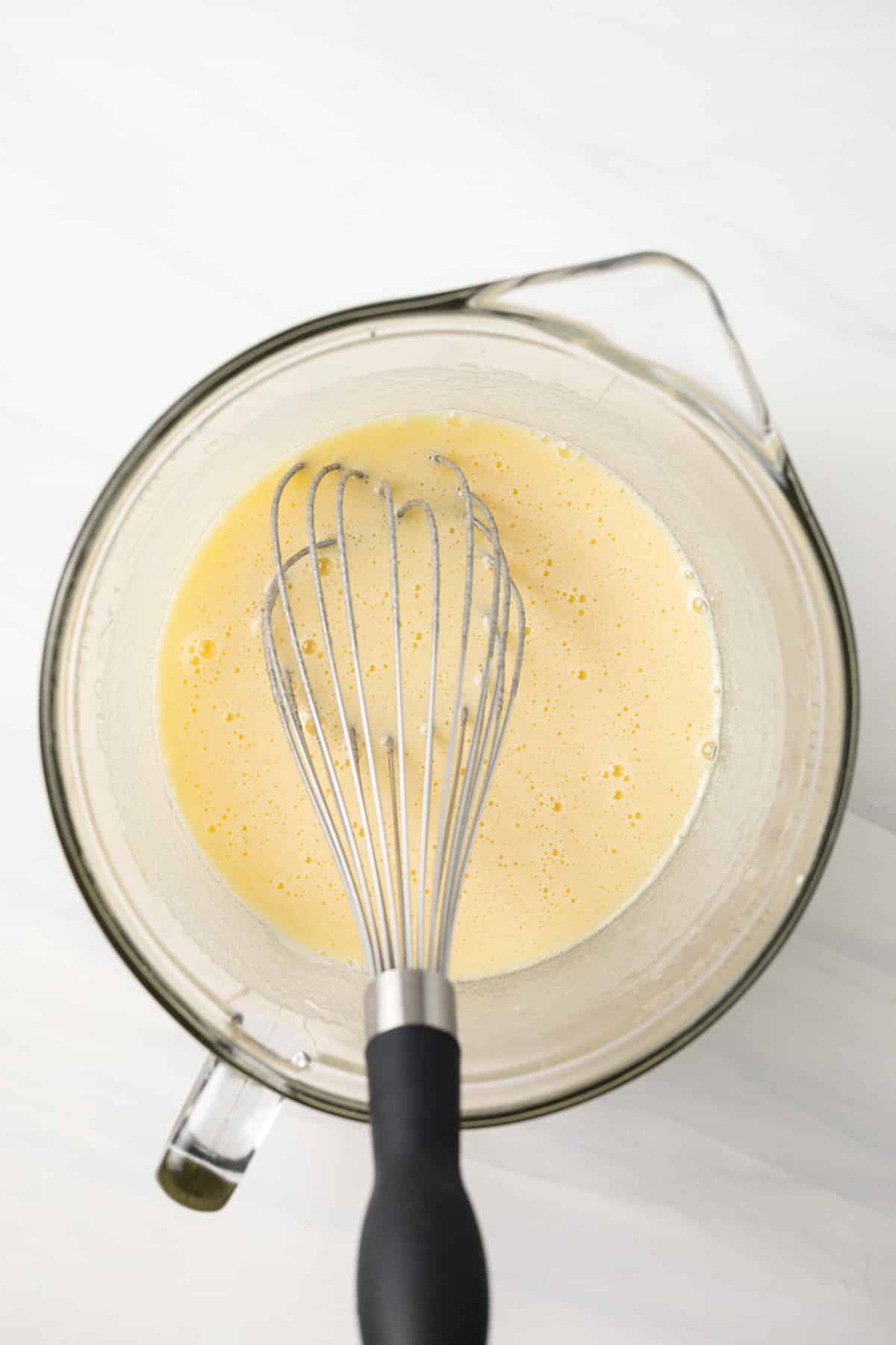 Eggs and sugar whisked in a glass bowl.