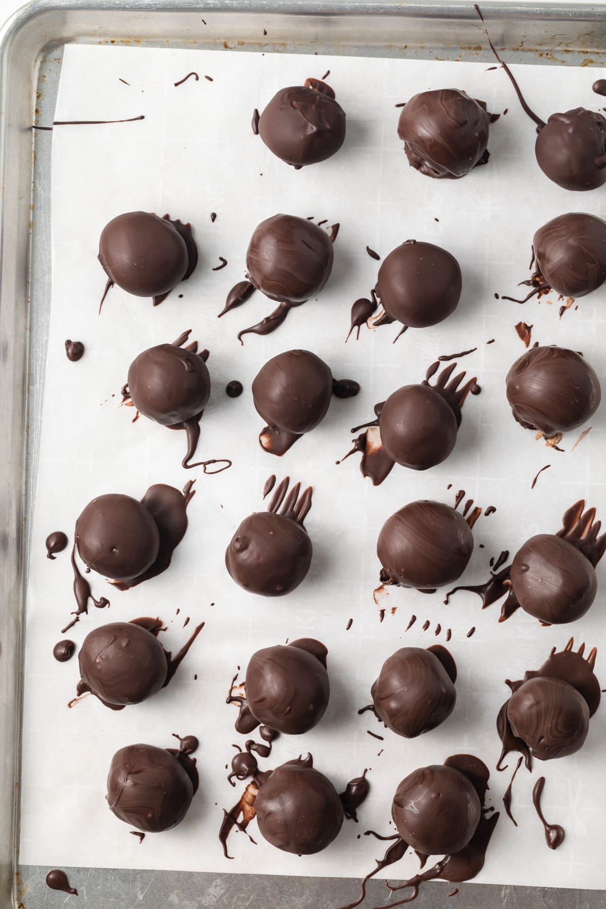 Chocolate coated peanut butter balls on baking sheet.