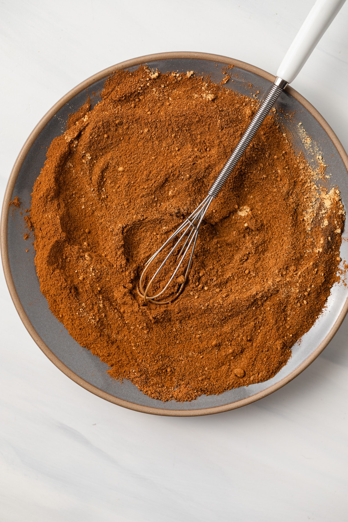 Pumpkin pie spice mixed on a plate with a small whisk.