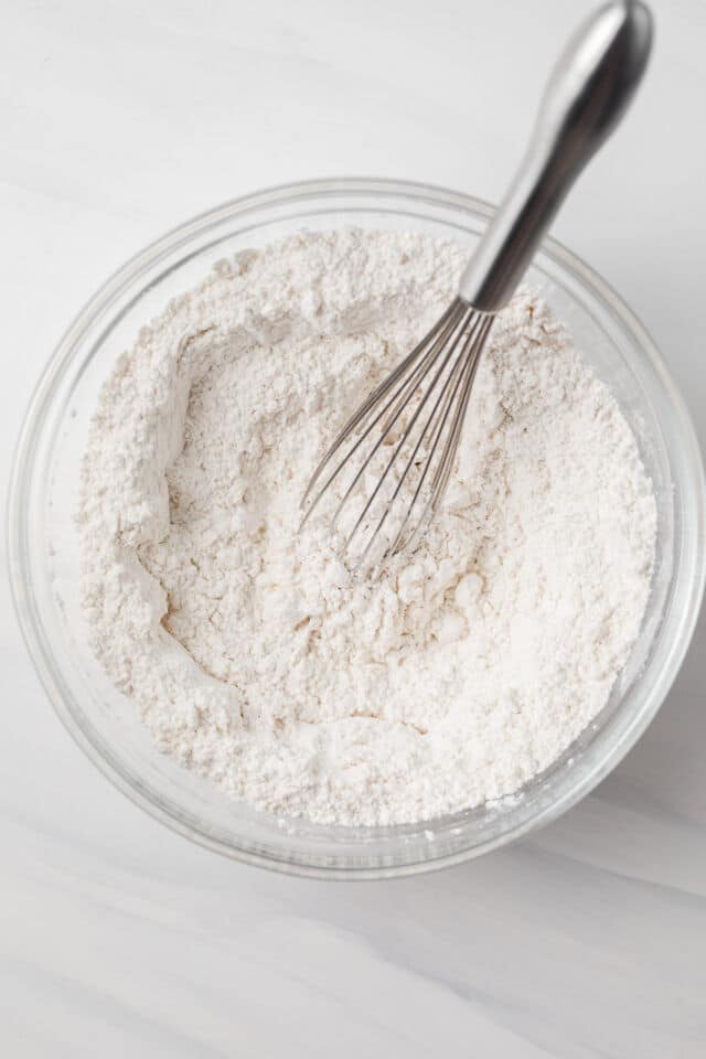 Dry ingredients in a glass bowl with a whisk.