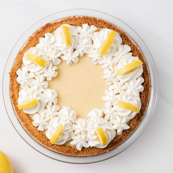 Overhead of lemon pie topped with whipped cream and lemon wedges.