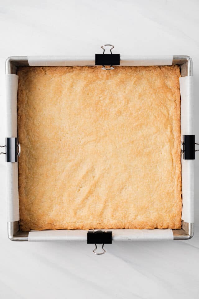 Baked shortbread layer in square baking pan.
